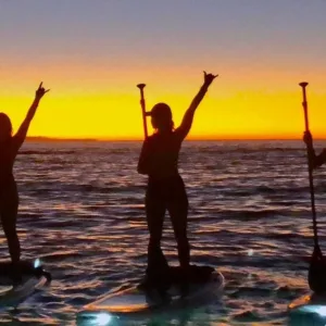 People paddleboarding on ocean at dusk