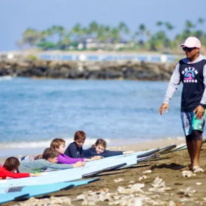 Group of five surfers listening to instructor on beach